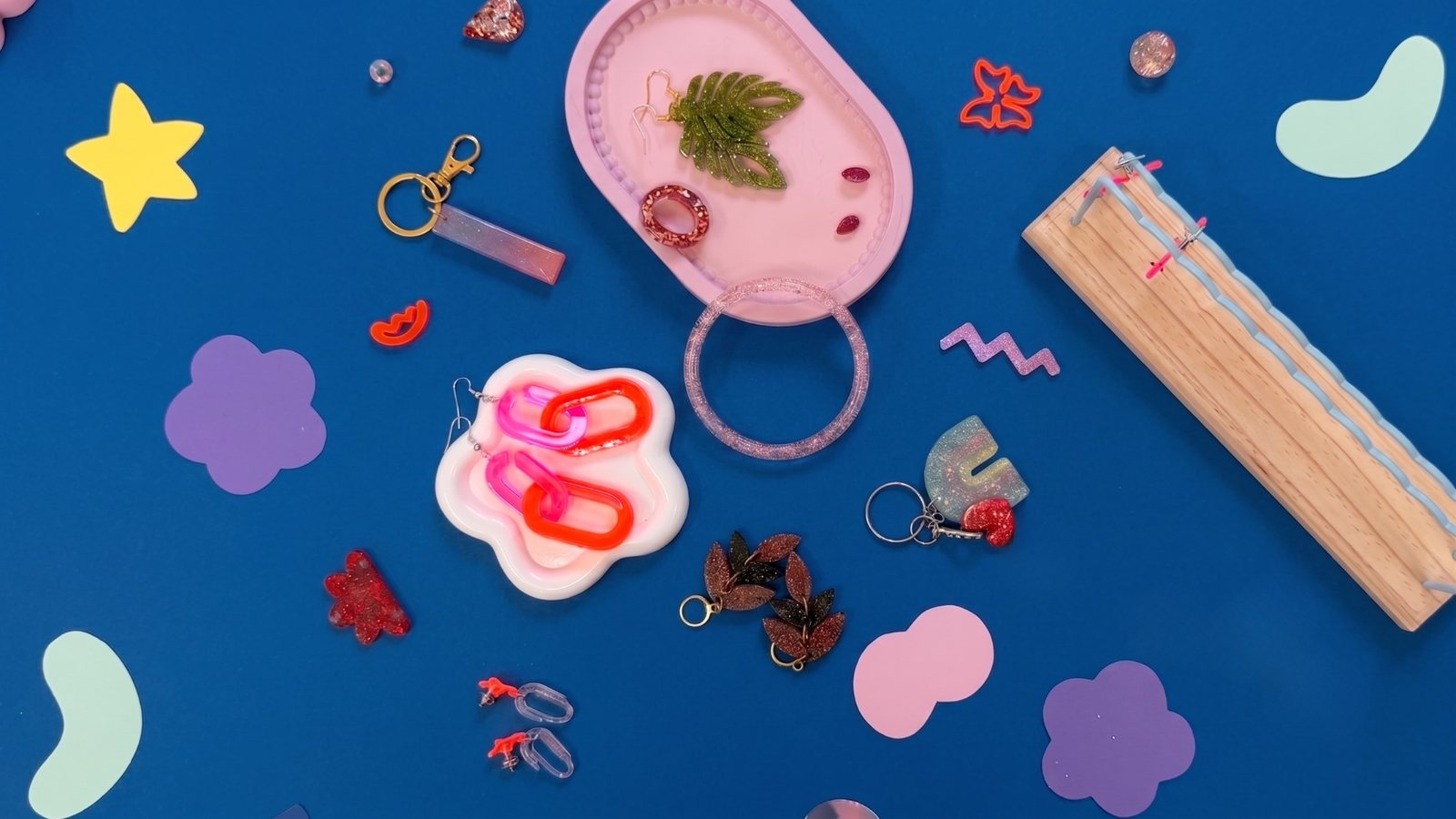 Selbstgemachter Schmuck aus UV-Resin: Ohrringe in Blattform und mit Kettengliedern, Glitzer-Armreif, Ring und Schlüsselanhänger auf einem rosa Tablett