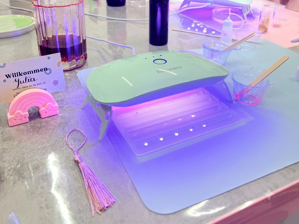 Workshop-Moment: ein Lesezeichen härtet unter der violett leuchtenden UV-Lampe aus, daneben eine Willkommenskarte und eine Quaste