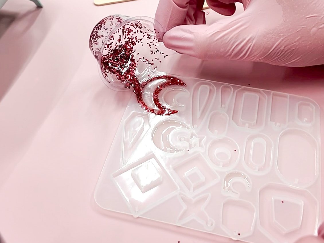 Workshop-Moment: mit Handschuhen wird rot glitzerndes UV-Resin in eine Silikonform mit Schmuck-Aussparungen gegossen