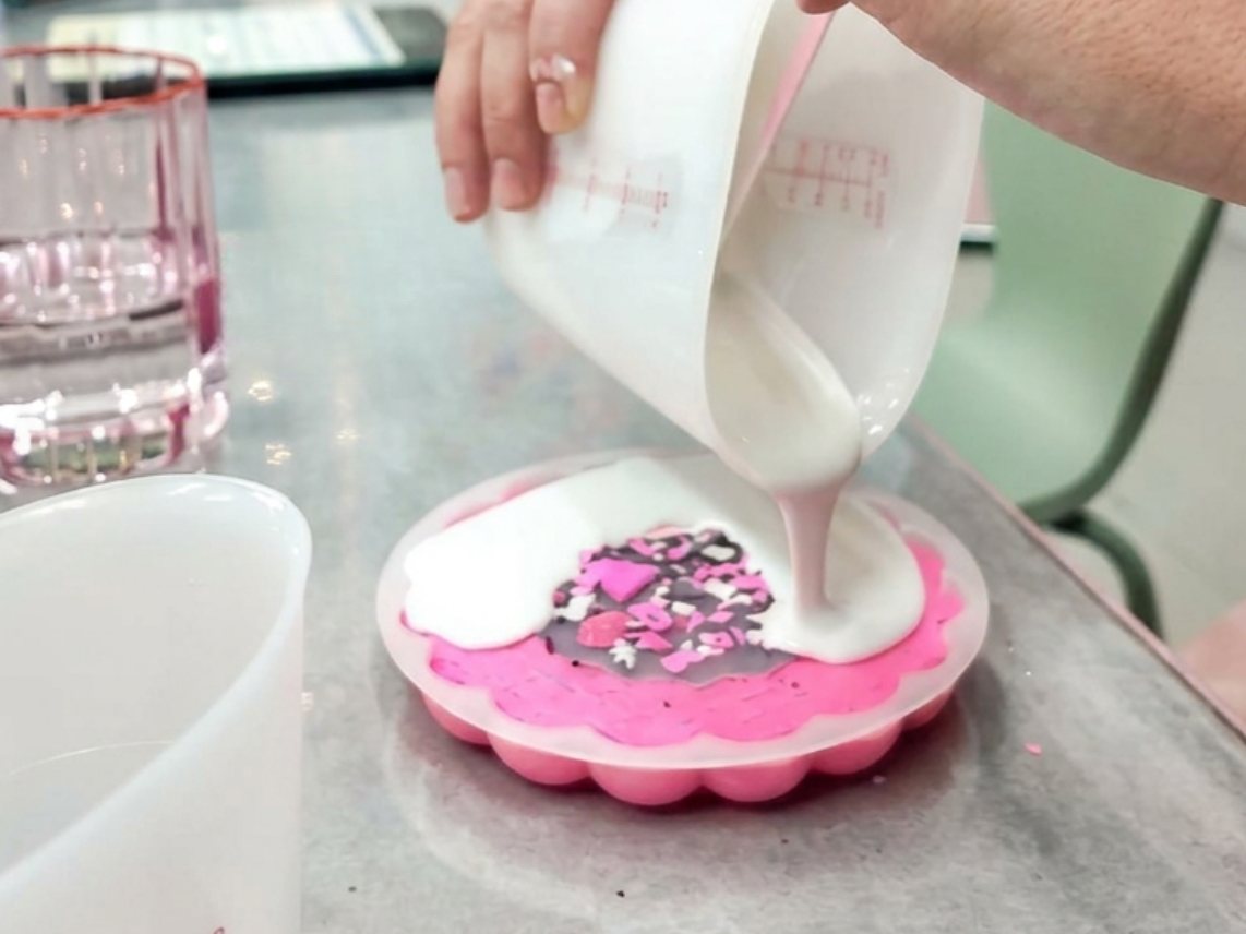 Workshop-Moment: flüssiges Raysin wird aus einem Messbecher in eine rosa Silikonform mit Terrazzo-Einschlüssen gegossen